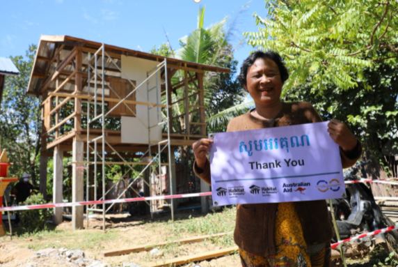 Chann - a grandmother in Cambodia holding a sign in front of her new home in Cambodia - Habitat for Humanity