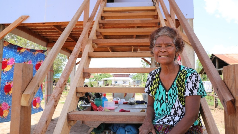 A photo of homeowner Lean sitting on the wooden steps of her home in Cambodia. She's smiling.