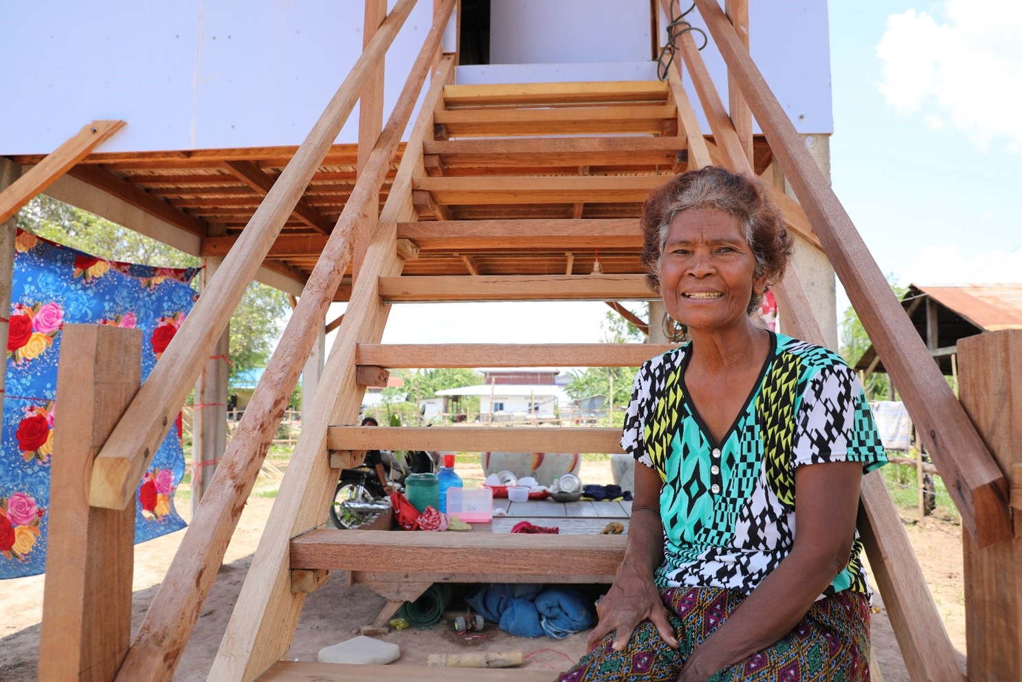 A photo of homeowner Lean sitting on the wooden steps of her home in Cambodia. She's smiling.