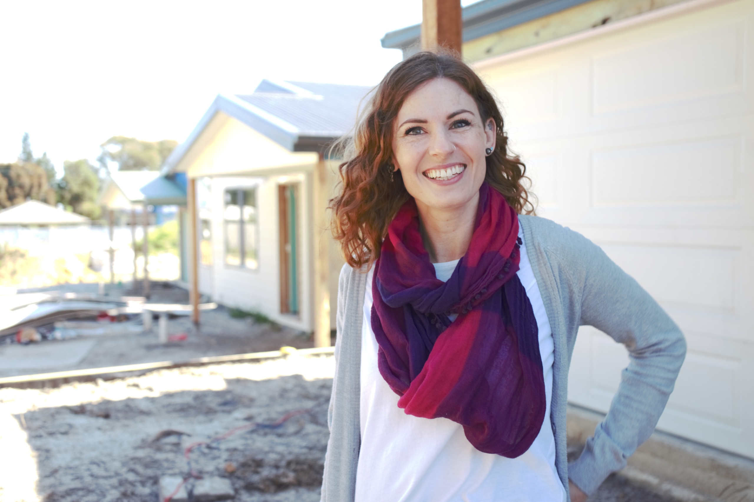 A photo of a woman smiling as she stands in front of a nearly completed house build