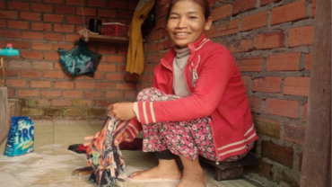 A smiling woman, Sophay crouches on the soapy, tiled floor of her new washroom, doing her laundry.