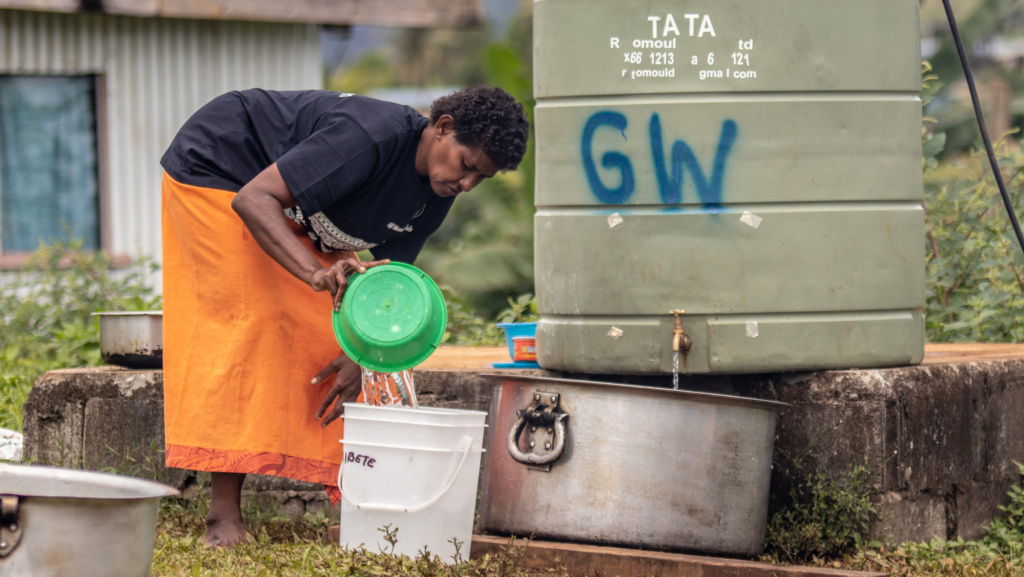 A Fijian woman collects water into a bucket from a water tank. 