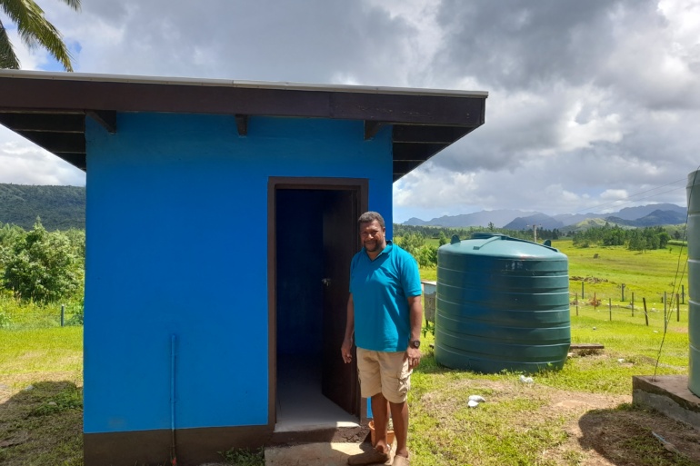 A man stands outside a newly constructed WASH facility, which can be used for Menstrual Hygiene at the Nalaba School.