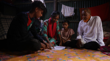 A family sit together on the floor in an informal settlement in Dhaka, Bangladesh