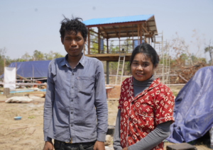 Savuth and Luch stand smiling outside their new home, built by Habitat for Humanity