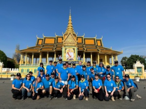 30 volunteers wearing blue Habitat shirts sit in front of a Cambodia temple