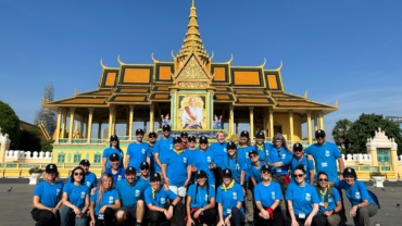 30 volunteers wearing blue Habitat shirts sit in front of a Cambodia temple
