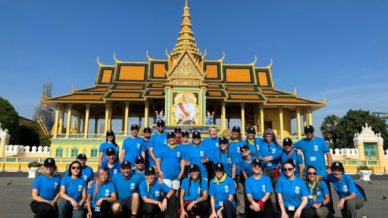 30 volunteers wearing blue Habitat shirts sit in front of a Cambodia temple