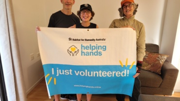 Three volunteers stand holding up a sign stating 'Helping Hands' 'I Just Volunteered'