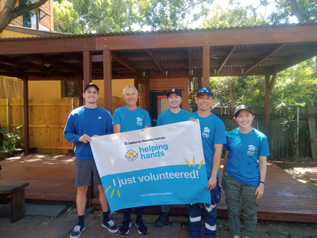 Lavinia stands in the center of the image alongside four other habitat volunteers. They hold up a sign stating 'helping hands' 'I just volunteered!'