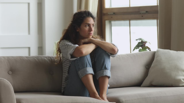 A woman sits on a couch looking sadly into the distance