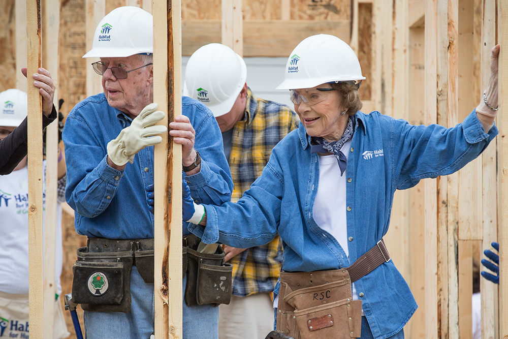 President Carter and Mrs Rosalynn Carter hold a timber beam on a building site.