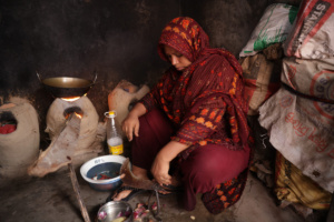 Sumi sits on the floor surrounded by bowls and utensils. She is making dinner.