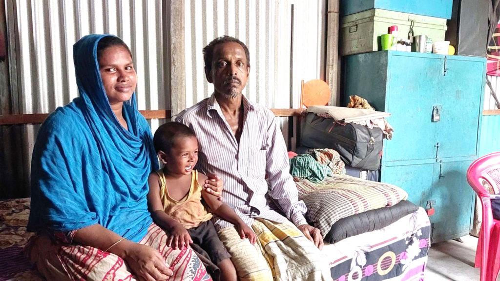 Monir sits with his wife and child in their home in Dhaka
