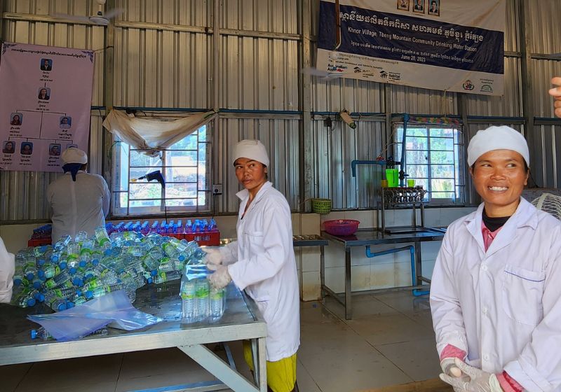 three women stand in PPE working at the water station