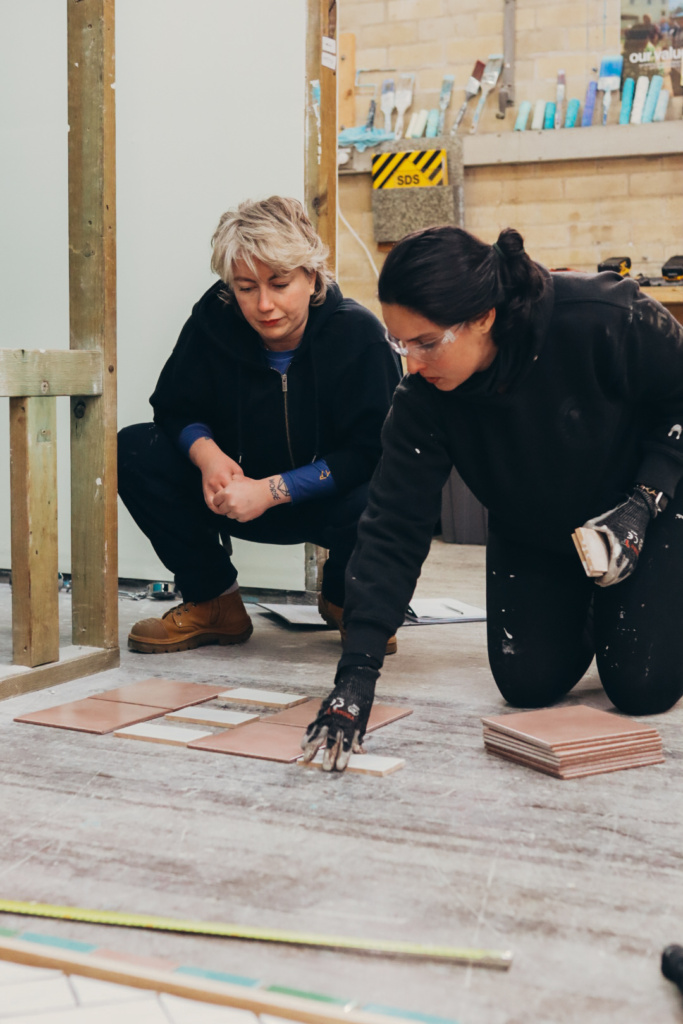 Carolina and another member of Habitat Women create their tile design on the workshop floor. 