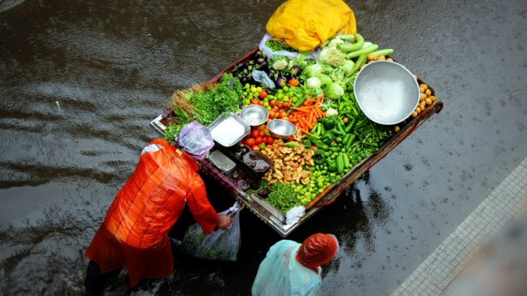 two men push a wooden cart of fresh produce through flood water